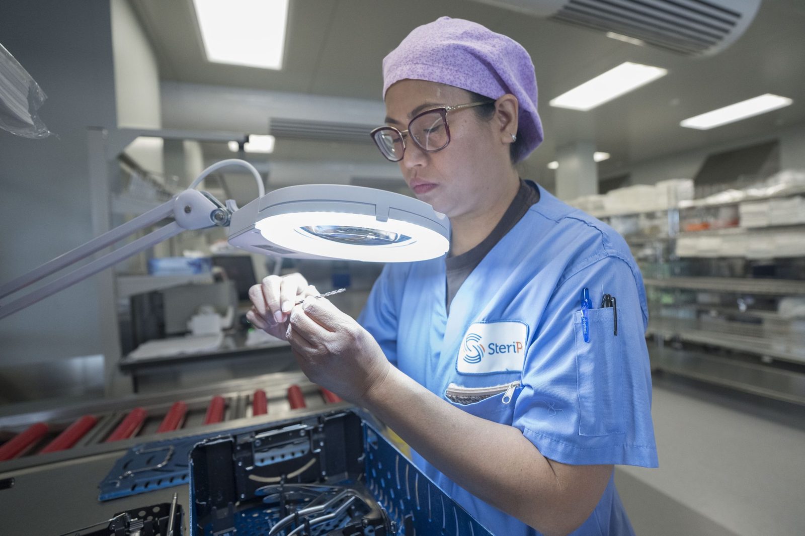 SteriPro technician inspecting surgical instruments under a magnifier lamp at an assembly station