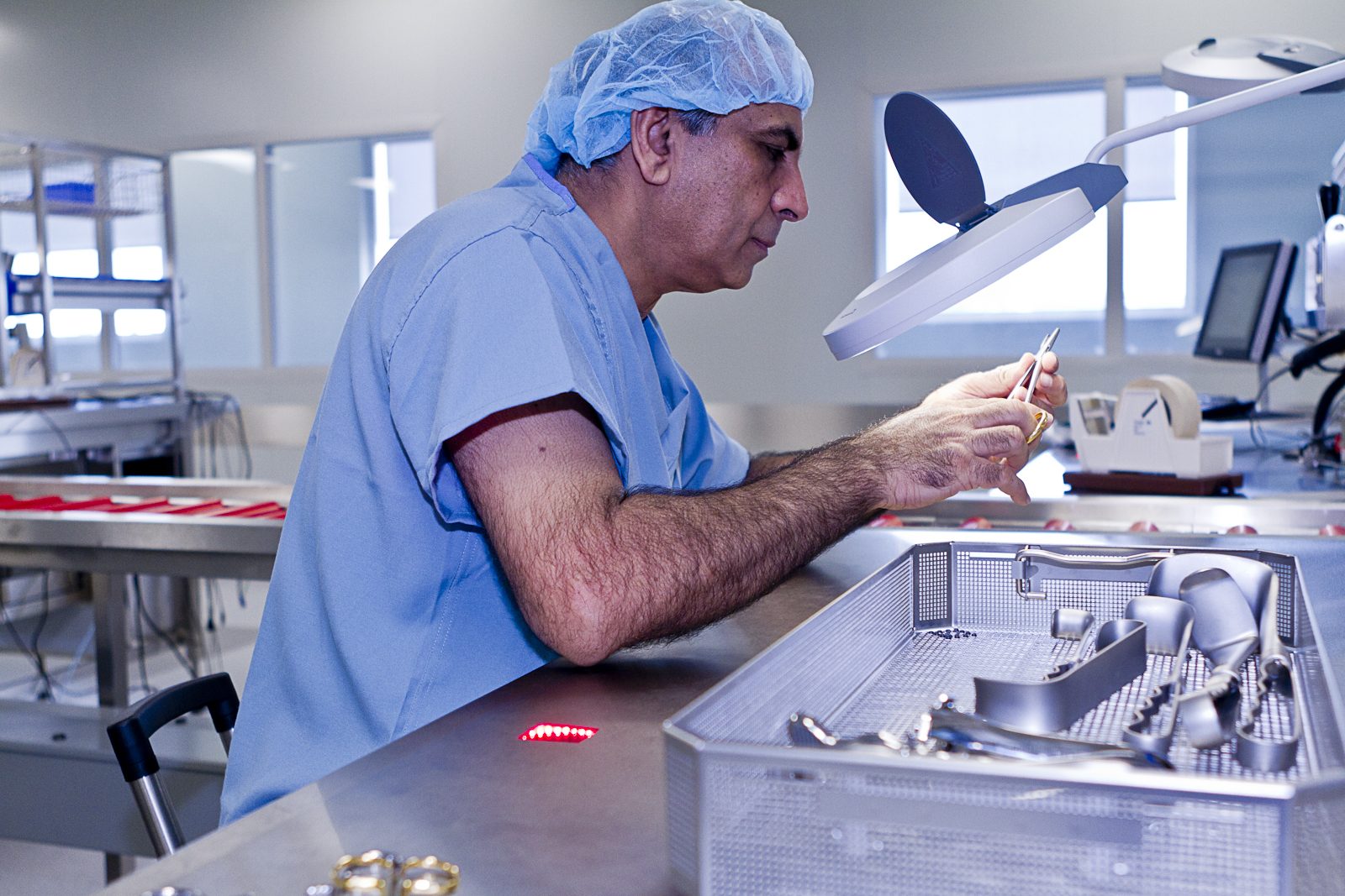 SteriPro technician inspecting surgical instruments under a magnifier lamp at an assembly station